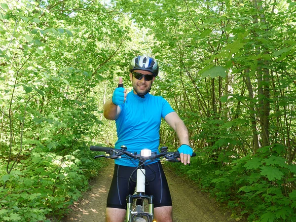 Hombre feliz montando una bicicleta de montaña en el bosque verde . — Foto de Stock