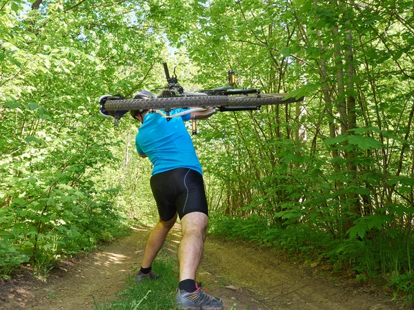 Ciclista homem carrega bicicleta na floresta verde no verão . — Fotografia de Stock