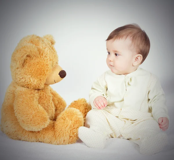 Niño pequeño sentado junto a un osito de peluche — Foto de Stock