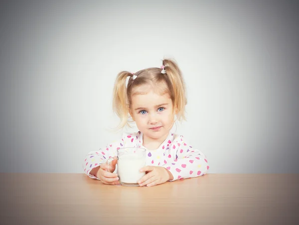 Glad liten flicka med ett glas mjölk. Stockbild