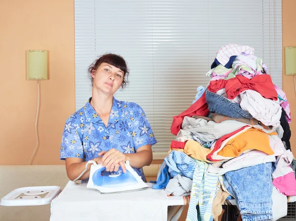 Young Caucasian woman ironed clothes in the room near  window.