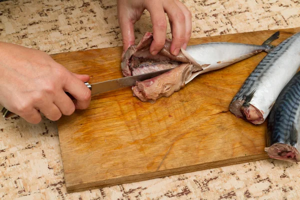 Nainen kokki viipaloi kala mackrel puulaudalla — kuvapankkivalokuva
