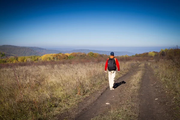 Turista masculino com mochila está em uma estrada rural — Fotografia de Stock