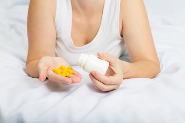 woman in her pajamas in bed holding yellow pills clipart