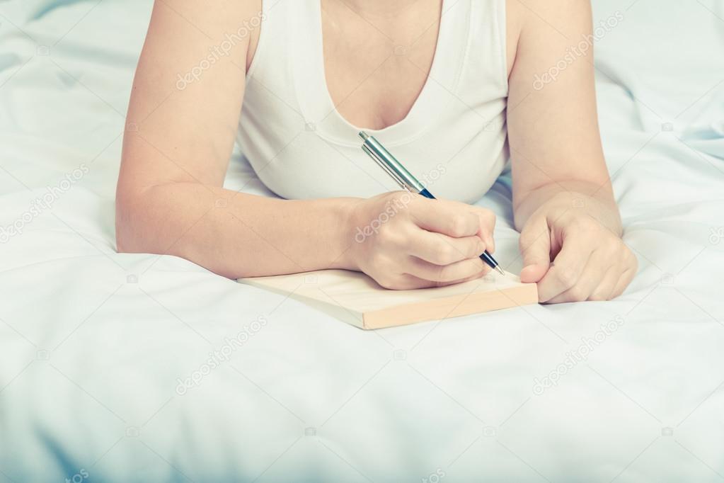 Young woman on bed with notebook. 