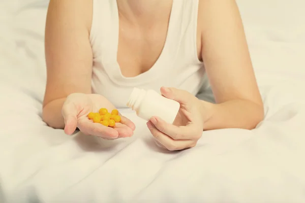 Женщина в пижаме в постели держит желтые таблетки — стоковое фото