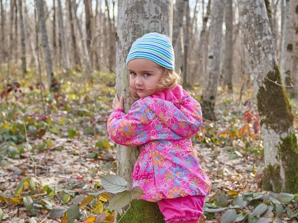 Söt liten flicka kramar en trädstam i vårskogen. — Stockfoto