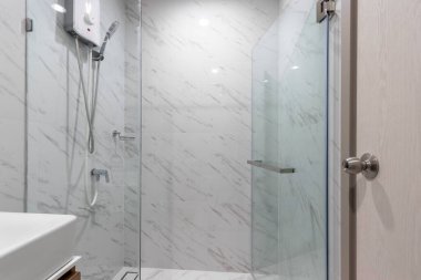 Su ısıtıcısı ve duş kabini olan küçük beyaz bir banyo. 