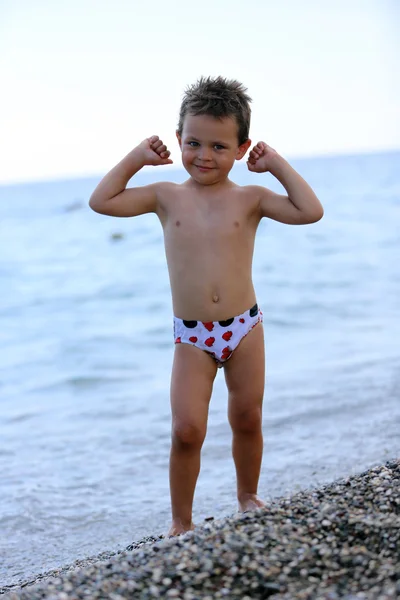 Jongen op het strand laat zien hoe sterk hij is Stockfoto