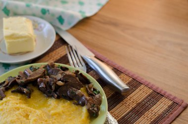 Mısır lapası, kızarmış mantar, soğan ve tereyağı. Geleneksel ev yemeği. Masa takımı mutfak masasında.. 