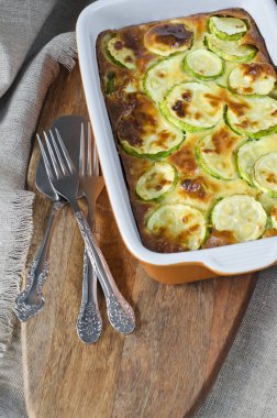 Kabaklı güveç ve ahşap kesim tahtasının üzerinde seramik bir fırın kabında peynir..