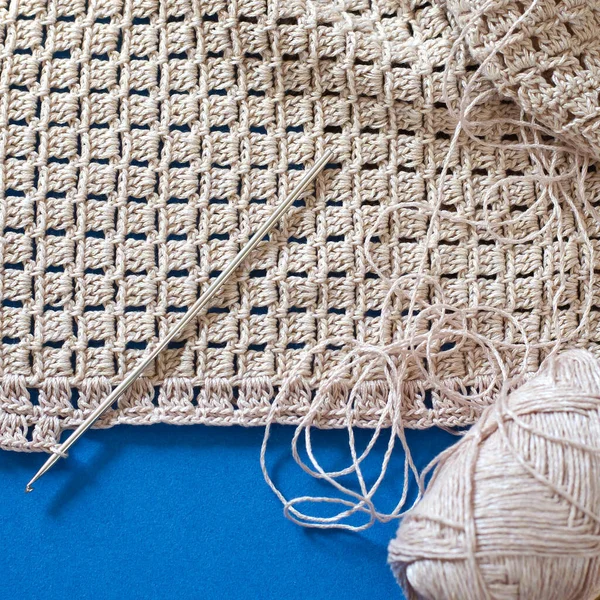 Crochet with beige cotton threads on a blue background. Simple crochet pattern.