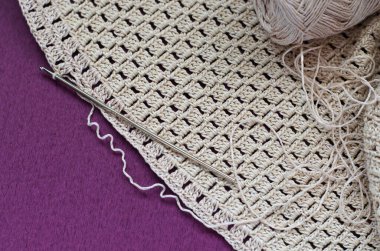 Mor bir arka planda bej pamuklu örgü. Basit tığ işi deseni. 