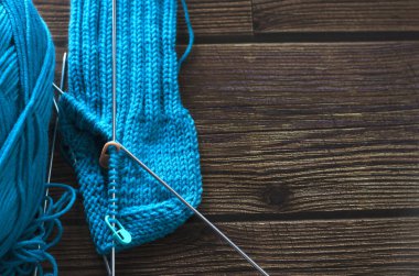 Örgü iğnelerinin üzerine mavi yün iplikten sıcak bir çorap örüyorum. Örgü projesi devam ediyor. Kahverengi ahşap masa. Üst görünüm.