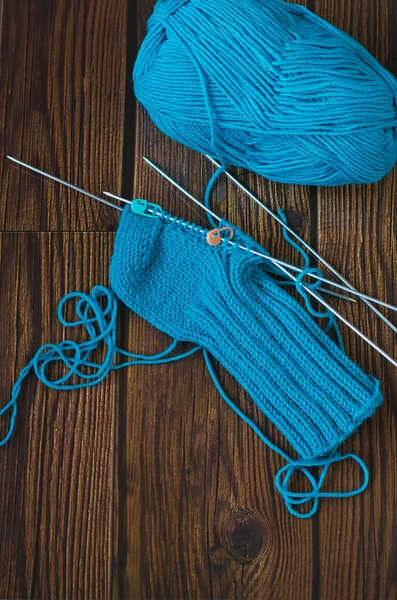 用蓝色毛线在针织针头上编织一个温暖的袜子 编织项目正在进行中 棕色木制桌子 顶部视图 — 图库照片