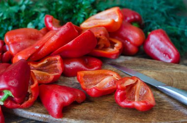 Çiğ kırmızı dolma biber, ikiye bölünmüş ve tahta kesme tahtasında maydanoz. Ahşap arka planda dilimlenmiş kırmızı dolma biber. Sebze, malzeme ve temel gıdalar. Faydalı yemek..