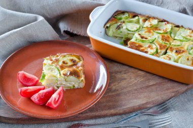 Ağaç kesme tahtasının üzerinde kabak ve peynirli ev güveci. Kahverengi seramik tabakta kabak güveci servis ediliyor. Beslenme, düşük kalorili fitness gıdası.