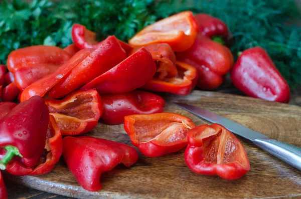 Raw red bell pepper, chopped in half and parsley on a wooden cutting board. Sliced raw red bell pepper in a wooden background. Vegetable, ingredient and staple foods. Useful food.