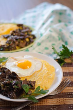 Mısır lapası, kızarmış yumurta, hasır bambu peçetede soğanlı kızarmış mantar. Geleneksel ev yemeği. Masa takımı mutfak masasında..