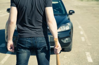 Man with baseball bat on the road before the car