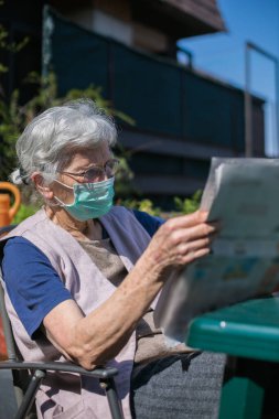 Coronavirus salgını sırasında terasta gazete okuyan yaşlı kadın.