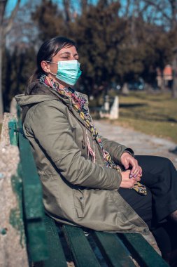 Yüz maskeli kadın parkta tek başına oturuyor.
