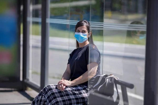 Kvinde Med Ansigtsmaske Sidder Ved Busstoppestedet - Stock-foto