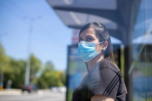 woman with face mask sitting at bus stop and waiting for a bus