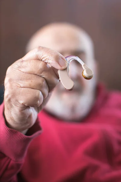 old man holding hearing aid in hand