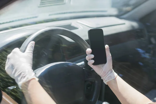 スマートフォンを手に持ちながらラテックス製の手袋で車を運転する — ストック写真