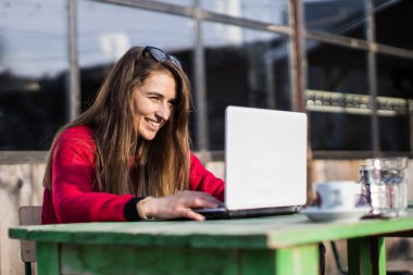 Gülümseyen kadın dışarıdaki kahve masasında dizüstü bilgisayarda çalışıyor.