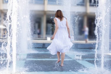 Genç bir kadın yaz sıcağında çeşme suyunda serinliyor.