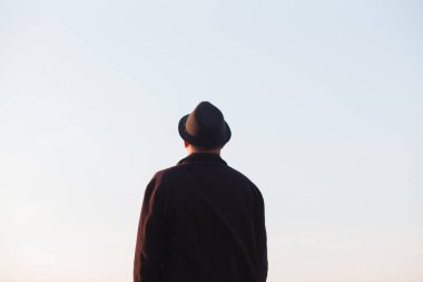 Şapkalı adam açık gökyüzüne bakıyor.