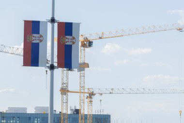 Arkaplanda inşaat vinçleri bulunan bir direkte Sırp bayrakları sergilendi