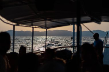 Yolcular gün batımında bir tekneden kıyı dağlarını görürler.