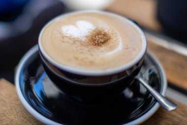 Sabah saatlerinde sıcak bir kafede üzerine tarçın serpilmiş siyah bir fincanda kremalı latte..