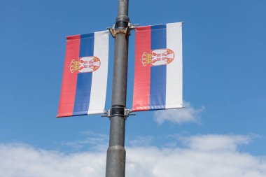 Gün boyunca açık mavi gökyüzünün altında bir sokak direğinde asılı Sırp bayrakları