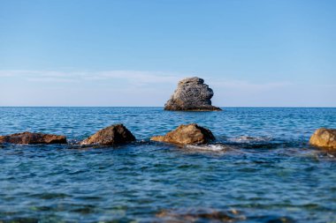 berrak bir gökyüzünün altında deniz suyundan çıkan bir sürü dev kaya.