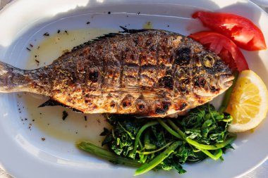 Gün batımında deniz kenarındaki bir restoranda taze sebze ve limonla servis edilen ızgara deniz kabuğu.