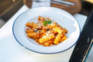 Taze fesleğen ve peynirle kaplanmış lezzetli rigatoni makarnası dışarıda sade bir masada servis ediliyor.