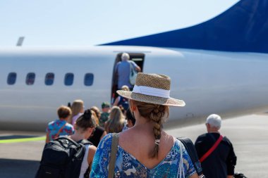 Güneşli bir günde havaalanında küçük bir uçağa binen yolcular
