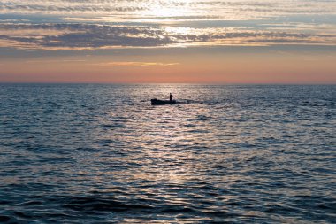 Gün batımında sakin sularda yüzen yalnız bir balıkçı sakin bir sahil kenarında.