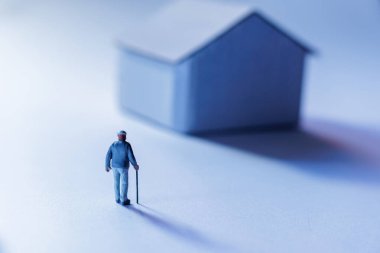 Bastonlu yaşlı adam figürü küçük model evin yanında duruyor.