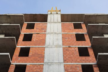 Açık mavi gökyüzünün altındaki kentsel alanda açık pencereli tuğla bina inşaatı