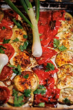 Kızarmış kabak ve yeşil soğanla süslenmiş kırmızı biber tabağı ve servis tepsisinde maydanoz.