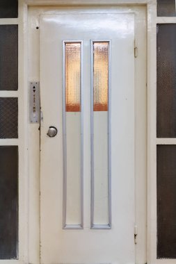 Tarihi bir bina koridorunda camları ve düğmeleri olan eski bir asansör kapısı.