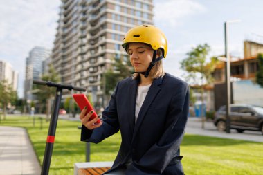 Açık havada akıllı telefon kullanan sarı kasklı bir kadın.