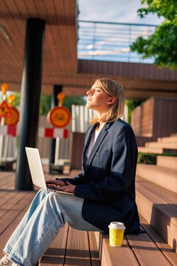 Dışarıda oturan bir kadın dizüstü bilgisayar kullanıyor ve dinleniyor.