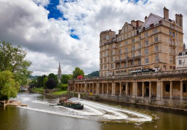 BATH, İngiltere - 11 Haziran 2013: Pulteney Köprüsü yakınlarındaki Empire Hotel ve arkada Parade Gardens parkı bulunan Avon nehri üzerindeki Pulteney Weir manzarası