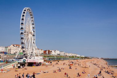 BRIGHTON, İngiltere - 5 Haziran 2013: Güneşli bir yaz gününde Brighton Sarayı İskelesi 'nden çekilen, Brighton Sahili boyunca dönme dolap ve turistle birlikte gezin.